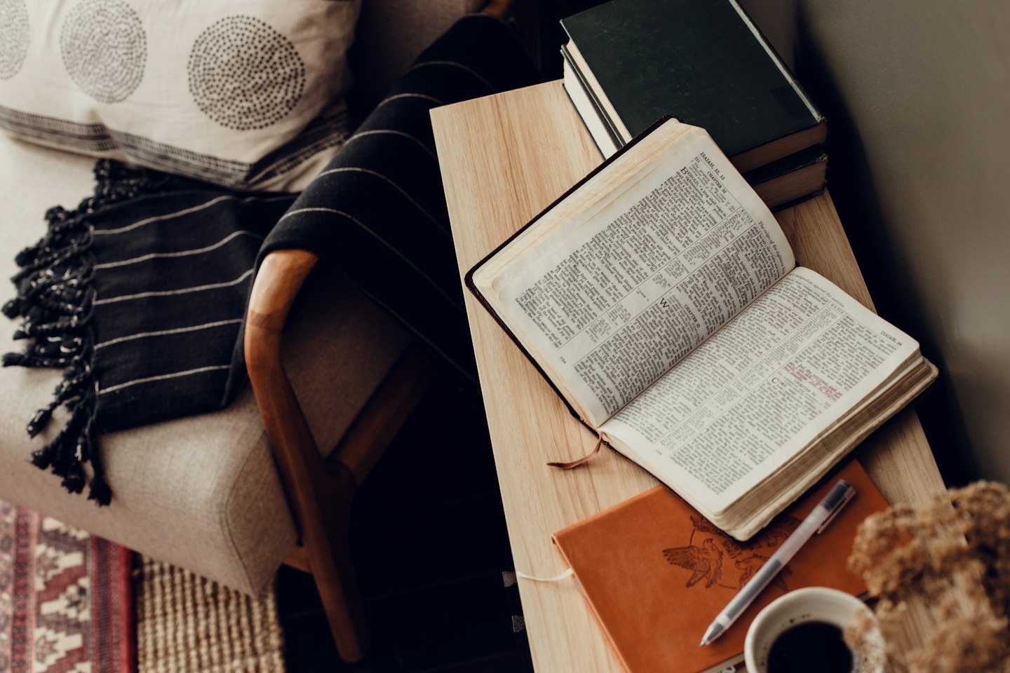 Open book and notebook on a wooden table near a sofa.