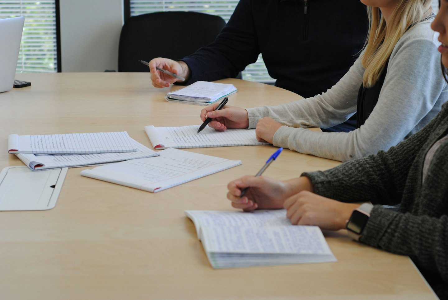 Three people collaborating and taking notes in notebooks.