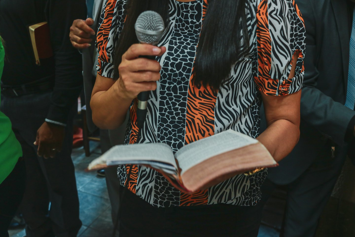 Person in patterned blouse reading from a book into a microphone.